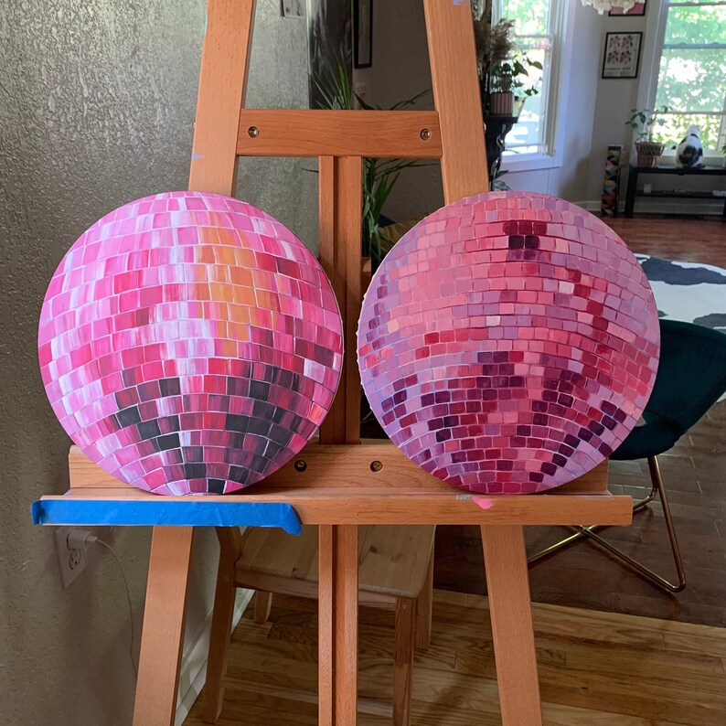 Pu&ograve; includere: Due dipinti rotondi di palle da discoteca, ciascuno composto da piccole tessere quadrate. Le palle da discoteca sono principalmente rosa, con variazioni di tonalit&agrave; che creano un effetto mosaico. Uno ha toni pi&ugrave; caldi, l'altro pi&ugrave; freddi. Sono esposti su un cavalletto di legno.