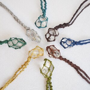 May include: Seven clear crystal pendants in macrame string holders. Each pendant is suspended from a different color cord: teal, brown, gray, green, yellow, navy, and white.