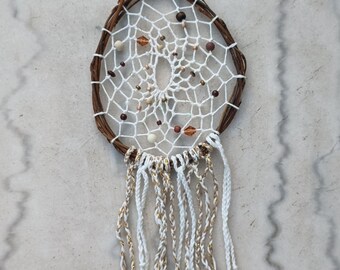 May include: A white dream catcher with brown twigs, white and gold beads, and white and gold tassels hanging from the bottom.
