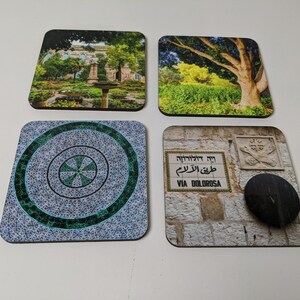 May include: Set of four square coasters featuring images of Jerusalem, Israel. The coasters feature a mosaic design, a tree, a building, and a street sign that reads "Via Dolorosa" in Hebrew and English.