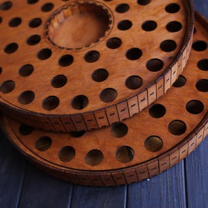 May include: Two wooden circular trays with a ring of evenly spaced holes around the outer edge. The top tray has a larger center hole. Both trays are a light brown color.
