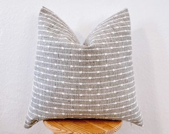 May include: A gray and white patterned throw pillow with a subtle geometric design. The pillow is sitting on a wooden stool.