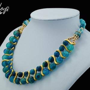 May include: A blue and green agate bead necklace with gold accents. The necklace is on a white mannequin bust.