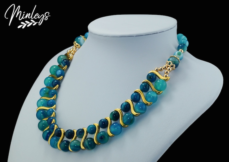 May include: A blue and green agate bead necklace with gold accents. The necklace is on a white mannequin bust.