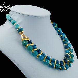 May include: A double-strand necklace with blue agate beads and gold accents. The beads are round and have a swirling pattern. The necklace is on a blue mannequin.