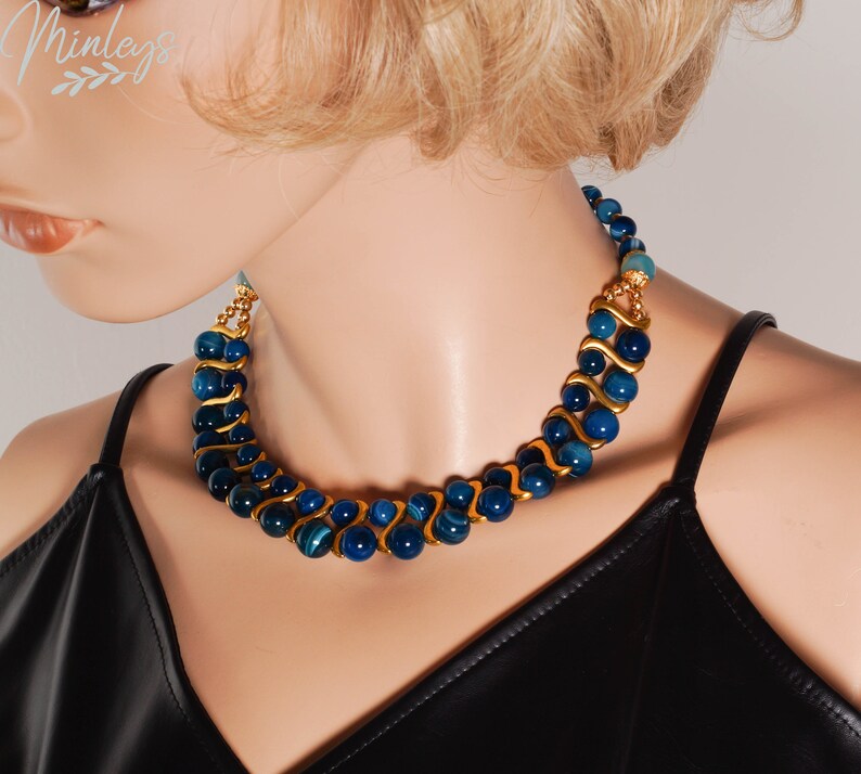 May include: A double-strand necklace with blue agate beads and gold accents. The necklace is on a mannequin wearing a black top.