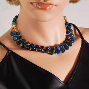 May include: A blue and gold necklace with a wavy design. The necklace is made of blue agate beads and gold metal.