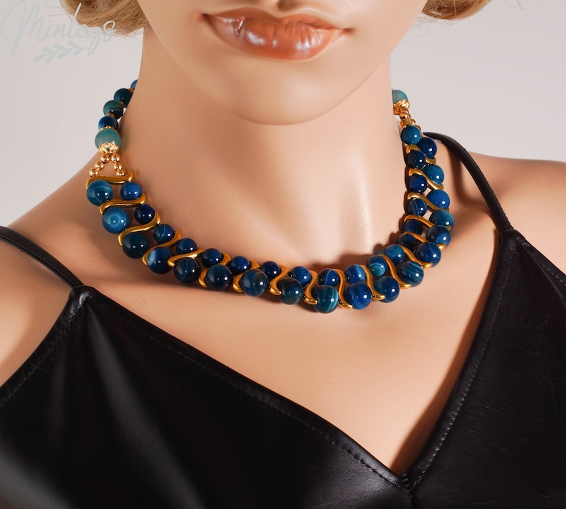 May include: A blue and gold necklace with a wavy design. The necklace is made of blue agate beads and gold metal.
