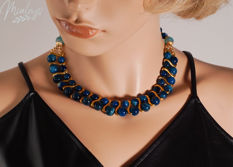 May include: A gold and blue necklace with a wavy design. The necklace is made of blue agate beads and gold wire.