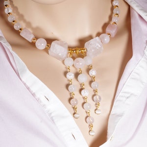 May include: A pink and gold necklace with a large, chunky rose quartz pendant and smaller rose quartz beads. The necklace has a delicate chain with small white beads and gold accents.