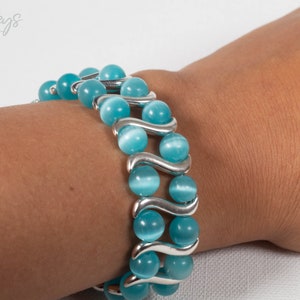 Op de afbeelding: Een turquoise blauwe kralen armband met zilveren accenten. De armband is gemaakt van ronde kralen en heeft een golvend ontwerp.