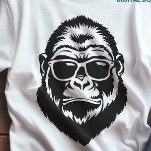 Puede incluir: Una ilustración en blanco y negro de un gorila con gafas de sol. La cara del gorila es el foco principal de la imagen, con las gafas de sol cubriendo sus ojos. La imagen está en una camiseta blanca.