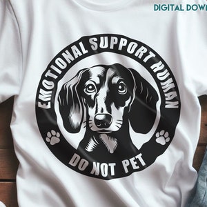 Peut inclure: Un t-shirt blanc avec un graphique noir et blanc d'un chien teckel. Le graphique dit "Emotional Support Human" et "Do Not Pet" avec des empreintes de pattes de chaque c&ocirc;t&eacute;.