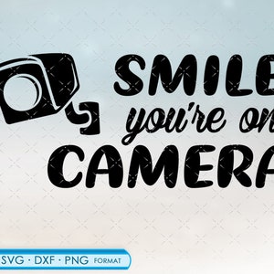 以下が含まれることがあります： セキュリティカメラと「笑顔で、あなたはカメラに映っています」というテキストが書かれた白黒のグラフィックデザインです。