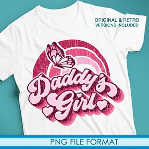 Op de afbeelding: Wit T-shirt met een roze en rood grafisch ontwerp met een vlinder en de tekst "Daddy's Girl" in een retro-lettertype.