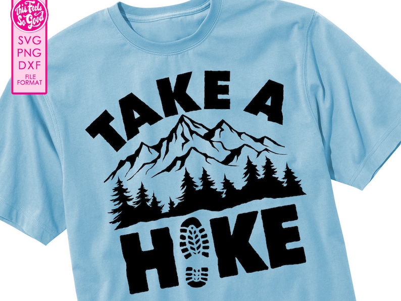 Op de afbeelding: Een lichtblauw t-shirt met een zwart grafisch ontwerp met de tekst "Take a Hike" met een bergketen en een voetafdruk.