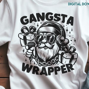 May include: A white t-shirt with a black graphic of Santa Claus wearing sunglasses and headphones, holding a microphone and a gift box. The text "Gangsta Wrapper" is printed below the image.