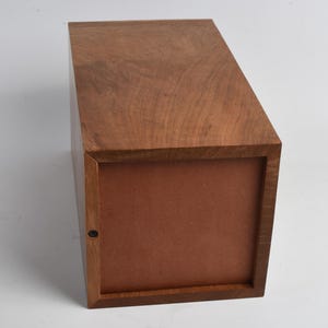 May include: A wooden box with a brown lid and a brown interior. The box is closed and sitting on a white surface.