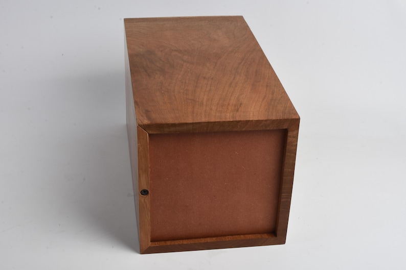 May include: A wooden box with a brown lid and a brown interior. The box is closed and sitting on a white surface.