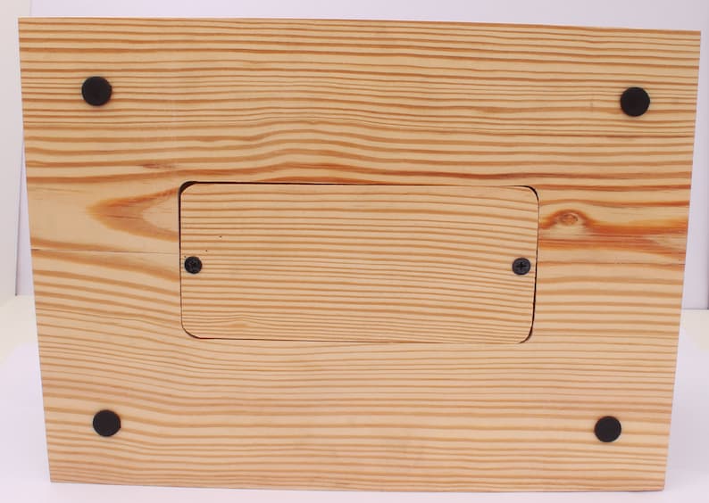 May include: A wooden box with a natural finish, featuring visible wood grain and a rectangular recessed area secured with two screws. Four black rubber feet are attached to the base for stability.