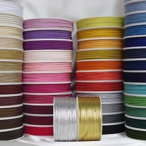 May include: A selection of spools of colourful waxed cord, including white, purple, pink, yellow, orange, red, blue, green, silver, and gold. The cords are wound around spools with white plastic.