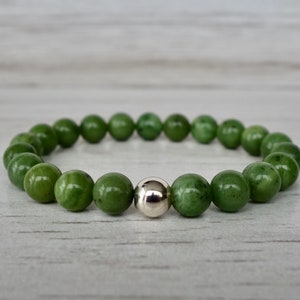 May include: A green jade stone bracelet with a silver bead accent. The bracelet is made of round beads and is approximately 7 inches in length.