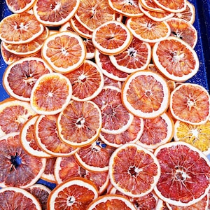 May include: A close-up of a blue tray filled with dried orange slices. The orange slices are arranged in a random pattern and are a vibrant orange color.