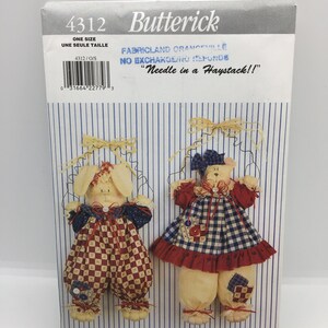 Może przedstawiać: Wzór szycia na dwa pluszowe króliki. Jeden królik ma na sobie niebiesko-białą kratkowaną sukienkę z czerwoną falbanką, a drugi królik ma na sobie niebiesko-czerwone kratkowane ogrodniczki. Wzór pochodzi od Butterick i nazywa się "Needle in a Haystack!"