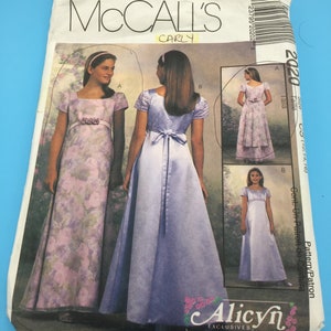May include: McCall's 2020 Carly pattern for a girls' dress. The pattern includes three different styles: a floral print dress with a sash, a solid blue dress with a sash, and a solid blue dress with a simple neckline. The pattern is for sizes 12, 14, and 16.
