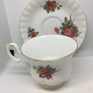 May include: A white teacup and saucer set with a gold trim and a floral design featuring red roses.