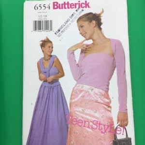 Peut inclure: Un patron de couture Butterick, numéro 6554, avec un design Teen Style. La couverture montre une femme en haut rose et jupe fleurie, et une autre en robe violette. Le patron comprend les tailles 1/2-7/8.