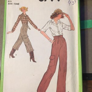 Op de afbeelding: Vintage Simplicity naaipatroon 8799. Het patroon toont illustraties van een vrouw in een geruit overhemd en cargobroek, en een andere vrouw in een wit overhemd en cargobroek. Het patroon is gelabeld "Miss Jeune Femme".