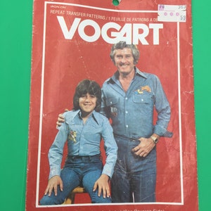 May include: A red and white package with the text "VOGART" in large white letters. The package contains iron-on transfer patterns for embroidery or ball point painting. The package features a photo of two people, a man and a boy, wearing blue shirts and jeans.