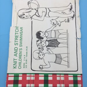 Op de afbeelding: Een vintage breipatroonboekje voor kinderbadkleding. De omslag toont een zwart-witte illustratie van kinderen in badpakken die spelen met een bal en een hond. De tekst op de omslag luidt "Knit and Stretch Children's Swimwear" en "Sizes: 2 to 6 U.S. $1.00 / Canada $1.25".