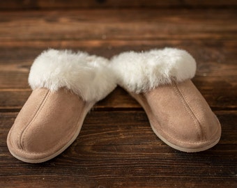 May include: A pair of brown suede slippers with white faux fur trim. The slippers are on a wooden surface.