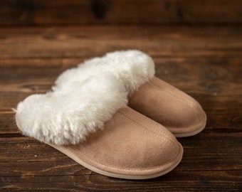 May include: A pair of brown suede slippers with white faux fur lining. The slippers are on a wooden surface.