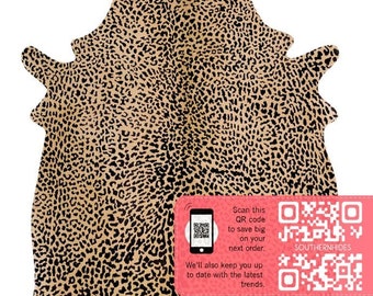 May include: A tan cowhide rug with a black leopard print pattern. The rug is shown on a white background. A pink and white square with a QR code and text is in the lower right corner. The text reads "Scan this QR code to save big on your next order. We'll also keep you up to date with the latest trends. SOUTHERNHIDES"