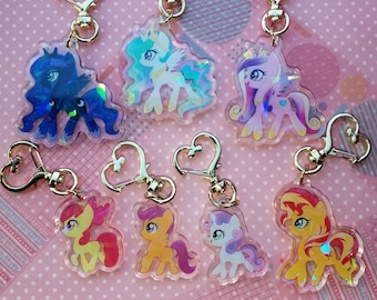 Könnte beinhalten: Sieben schimmernde Schlüsselanhänger mit verschiedenen My Little Pony-Charakteren. Jeder Schlüsselanhänger hat einen goldfarbenen Metallring und einen herzförmigen Verschluss. Die Charaktere sind Twilight Sparkle, Pinkie Pie, Rainbow Dash, Fluttershy, Rarity, Applejack und Prinzessin Celestia.