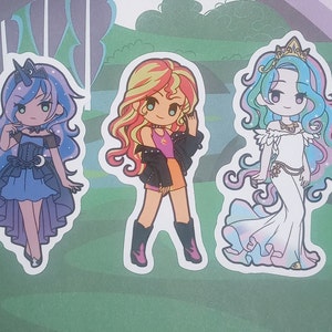 May include: Three cartoon character stickers featuring a blue and purple pony with a crescent moon, a yellow and orange pony with a red jacket, and a blue and pink pony with a white dress and a gold crown.