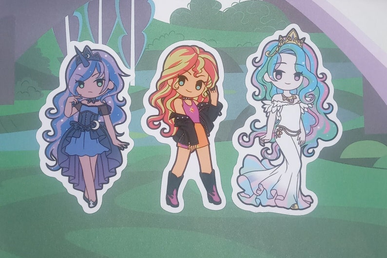 May include: Three cartoon character stickers featuring a blue and purple pony with a crescent moon, a yellow and orange pony with a red jacket, and a blue and pink pony with a white dress and a gold crown.
