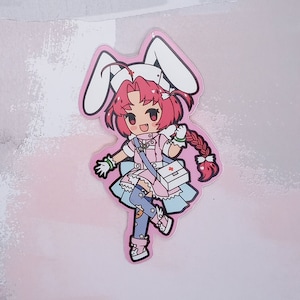 May include: A pink and white cartoon sticker of a girl with red hair wearing a nurse's outfit and bunny ears. She is holding a first aid kit and has a happy expression on her face.