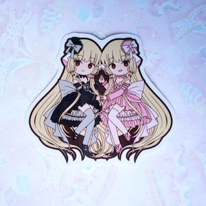Puede incluir: Una pegatina con dos figuras de estilo anime con largo cabello rubio y ojos rojos. Una figura lleva un vestido negro con un lazo, la otra un vestido rosa. Ambas figuras se dan la mano. La pegatina tiene un borde blanco.