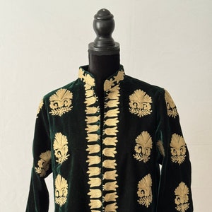 May include: A long, green velvet jacket with gold embroidery. The jacket has a mandarin collar and a button-up front. The embroidery features a floral pattern.