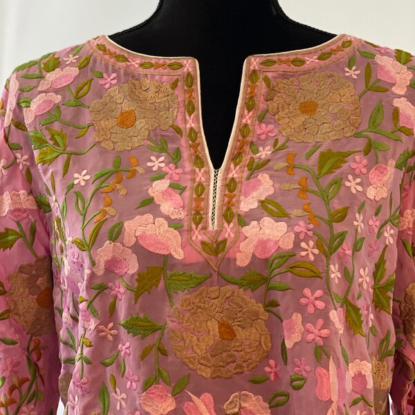 May include: A light pink, sheer tunic with a V-neckline and long sleeves. The tunic is embroidered with a floral pattern in shades of pink, green, and brown.