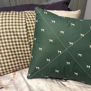 May include: Two decorative throw pillows. One pillow has a green and white plaid pattern. The other pillow is dark green with a white horse pattern. The pillows are on a bed with a floral patterned bedspread.