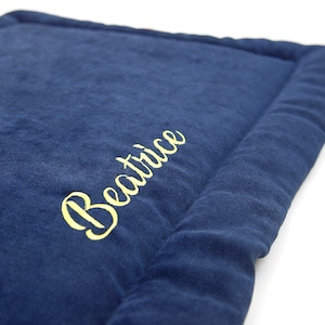 May include: A navy blue pet bed with a yellow embroidered name "Beatrice" on the top.