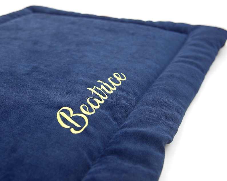 May include: A navy blue pet bed with a yellow embroidered name "Beatrice" on the top.