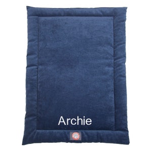 May include: A navy blue dog bed with a white border and the name "Archie" embroidered on the front. The bed has a red paw print logo in the bottom right corner.