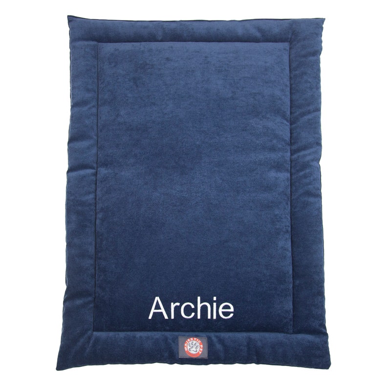 May include: A navy blue dog bed with a white border and the name "Archie" embroidered on the front. The bed has a red paw print logo in the bottom right corner.