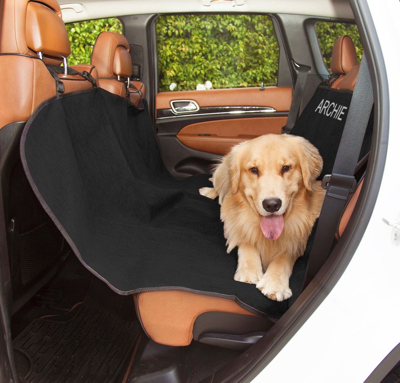 May include: Black car seat cover with the name "ARCHIE" embroidered on it. A golden retriever dog is sitting on the seat cover.